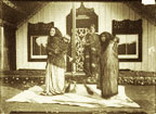 Photograph of Maōri women with babies on their backs standing in front of a meeting house. 